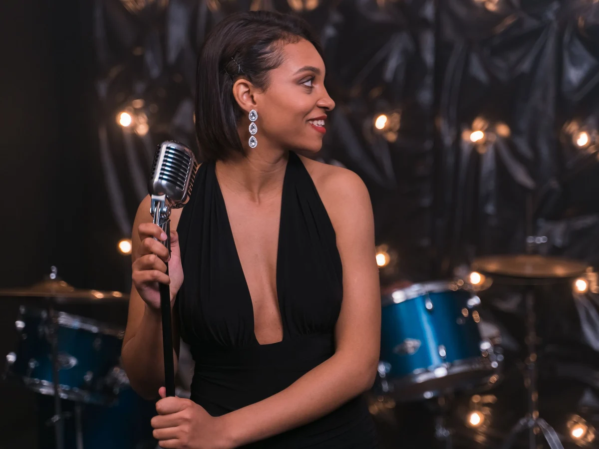 A singer in a black gown holding a vintage-style microphone, a drum kit visible behind her (representative photograph, not this venue's own cast)